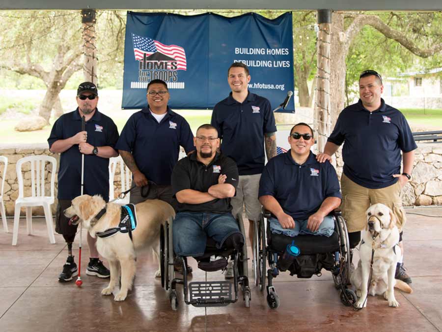 Photo of wounded veterans posing in front of the Homes for Our Troops banner